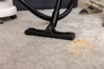 Black vacuum cleaner floor head labeled Kärcher on a light gray carpet with scattered orange crumbs nearby