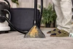 Carpet cleaning nozzle on a beige carpet, with a person wearing slippers standing nearby in the background.