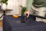 Person uses a handheld Kärcher cleaning nozzle on a dark blue sofa, cleaning crumbs from the fabric.