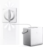 Window-cleaning robot attached to a glass pane with a circular cleaning head and a cord to a separate control unit.