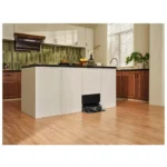 White kitchen island with a black countertop; a robotic vacuum cleaner sits under the island opening for docking and charging.