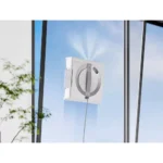 Wall-mounted glass-cleaning device with a circular wheel and gray arm attached to a large window pane