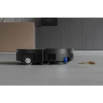 Robot vacuum cleaner moving across a grey floor near a cardboard box with a small spill nearby, indicating cleaning in progress.