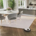 Robot vacuum cleaning a wooden floor in a modern dining-living room with a potted plant centerpiece.
