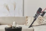 Cordless handheld vacuum cleaner being used on a beige sofa to clean upholstery.