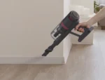 Cordless handheld vacuum being used to clean a wooden floor near the baseboard.