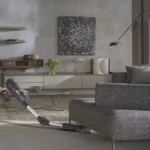 Person using a vacuum cleaner on a light rug in a modern living room with a gray couch and wall art nearby.