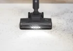 Vacuum cleaner head with LED lights cleaning scattered debris on a light floor.