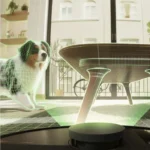 Dog in a bright living room looks at a circular smart device on the floor with a green holographic AR grid and a glass table nearby.