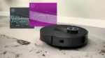 Black robotic vacuum cleaner on a light-gray floor with two floating map overlays showing cleaning progress and status icons (check and X).