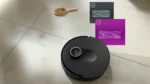 Robot vacuum on tiled floor with floating tutorial panels showing cleaning patterns or steps nearby.