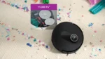 Circular robotic vacuum on a beige carpet with colorful confetti and party streamers, conveying a celebratory scene.