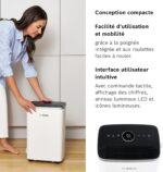 Woman operating a compact Bosch air purifier on the floor beside white cabinets in a home setting.