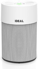 White cylindrical air purifier with a perforated silver grille and a green indicator on top, branded IDEAL, standing on a white surface.