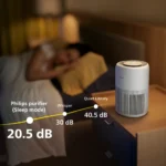 Air purifier on a nightstand in a dim bedroom with a sleeping person in the background; overlay shows noise levels: 20.5 dB (Sleep mode), 30 dB (Whisper), 40.5 dB (Quiet Library).