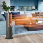 Tall gray space heater with a curved glass front on a round base in a modern living room, with orange light streaks across the scene.