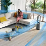 Child playing on a rug with yellow crane toys in a modern living room; blurred adult on sofa in background; blue airflow lines appear across the room from a tower fan in the foreground.