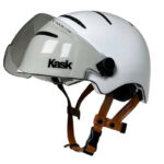 White cycling helmet with a clear retractable visor and brown adjustable chin straps, brand ‘Kask’ visible on visor.