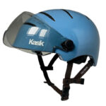 Blue Kask bicycle helmet with a clear, flip-down face shield and adjustable brown straps viewed from the side
