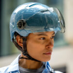 Young person wearing a blue hard helmet with a clear visor, looking to the right.