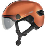 Copper-colored bike helmet with a clear flip-down visor and adjustable black chin strap.