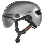 Silver bike helmet with clear visor and adjustable chin strap, showing Abus branding on the side.