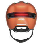 Orange Abus bike helmet viewed from the rear, showing a red rear light, logo, reflective strip, and adjustable chin strap