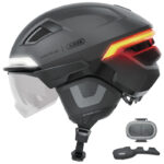 A dark gray bike helmet with built-in rear LED light, clear visor, and detachable ear pads for all-season use.