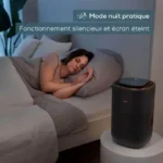 Woman sleeping on bed beside a cylindrical air purifier in night mode with the screen off and soft lighting.