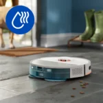 Autonomous robotic vacuum cleaning a tile floor beside scattered dry pet food pellets, with a blue circular icon featuring a water drop and steam overlaying the scene for emphasis.