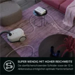 White canister vacuum on a pink rug with a dotted line showing a 12 m cleaning reach to a glass coffee table with books.