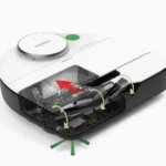 Cross-sectional view of a white robotic vacuum, showing the suction path, rotating brushes, and green side brushes inside.