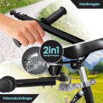 Hands gripping a bicycle handlebar with a 2in1 Transportwagen badge and hitch components nearby indicating a bike trailer accessory.