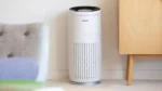 White cylindrical Bosch air purifier with a purple LED ring, standing on a tiled floor near a light wood cabinet.