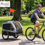 Man rides a bicycle while towing a grey PawHut dog trailer with a happy dog inside in a park.