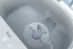 Interior of a top-loading washing machine with a central agitator and spindle visible in the tub center