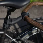 Close-up of a bicycle saddle mounted on a black seat post with a clamp and strap hardware visible.