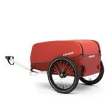 Red Croozer bike trailer with two large wheels and a front tow bar, designed to attach to a bicycle