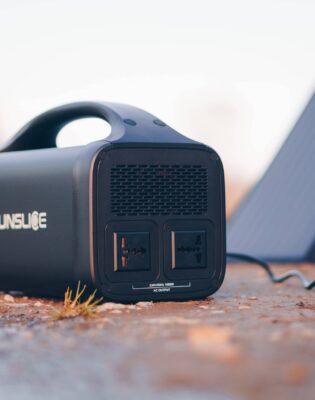 Portable power station with two outlets and handle, outdoors near a solar panel setup on the ground