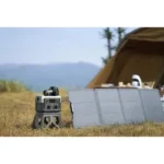 Camera on a small tripod beside a foldable solar panel at a sunny campsite, with a tent in the background.