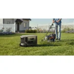 Person mowing a front yard with a portable generator on the grass nearby for power.",