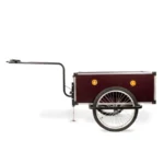 A vintage-style bicycle trailer with a dark red box, single rear wheel, and long tow bar attached at the front.