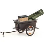 Towable utility wagon with a hitch, two wheels, and a raised green ramp/bag at the back, loaded with stacked wooden toolboxes.