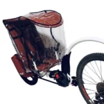 Red child bike trailer with a clear rain cover attached to a bicycle wheel.