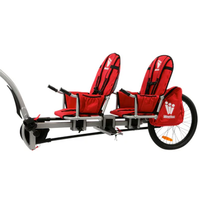 Red two-seat child bike trailer with harnesses and red seats, hitched to a bicycle for riding with kids.