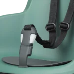 Close-up of a black harness strap with a gray buckle clipped to a green molded surface (child seat/adapter)