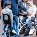 Two kids ride bicycles with an adult assisting between them, one wearing a helmet labeled 'one' on the left.