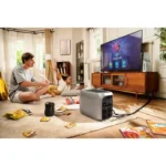 Portable power generator powers a TV in a cozy living room where a man and child play on the floor with snacks nearby.
