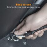Close-up of a hand attaching a metal D-ring and strap inside a vehicle to secure cargo