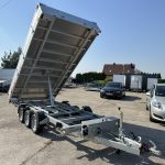 Hydraulic tilt-bed trailer with its bed raised at an angle in a parking lot, showing multiple axles and loading ramp area.